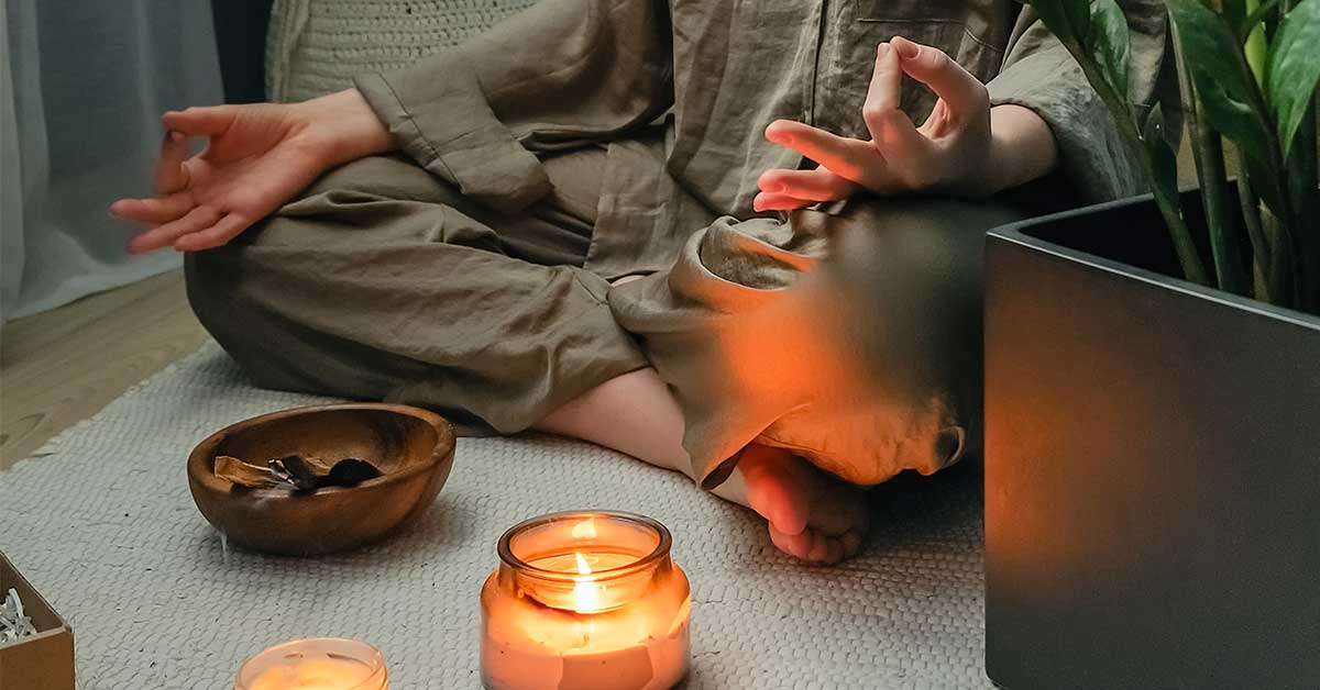 Person sitting cross-legged on a mat in a meditative pose, with a lit candle, bowl, and potted plant nearby—embracing self-improvement and clearing myths about intuition through mindful practice.