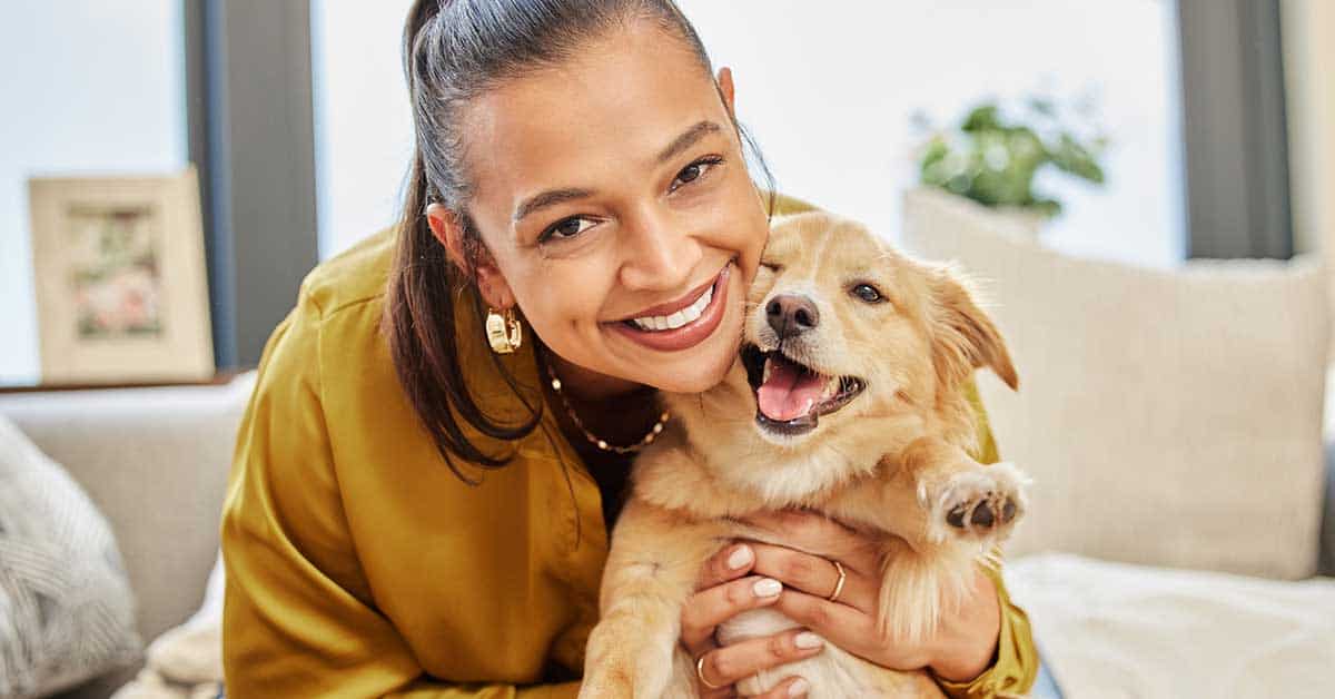 A person beams with joy, cradling a happy puppy indoors, the embodiment of pet wellness and boundless energy.